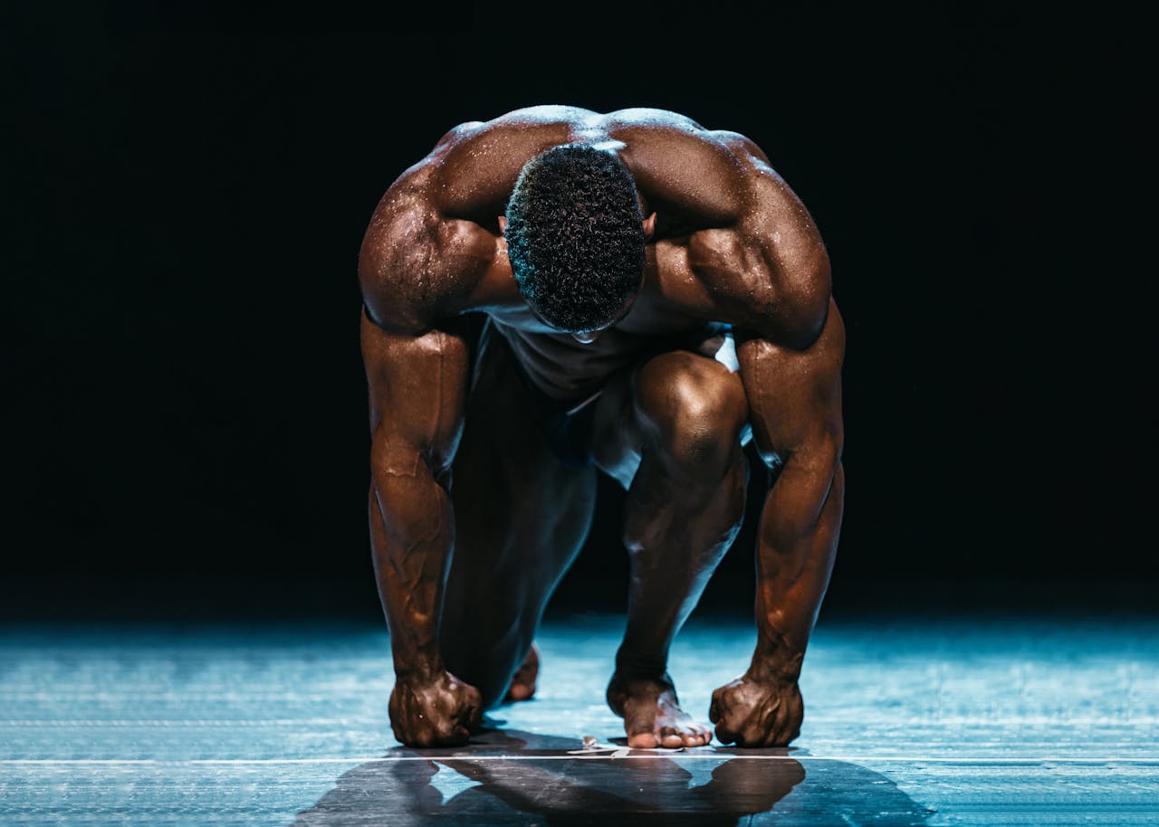 Muscular athlete in a powerful starting position on a dark, dramatic stage.