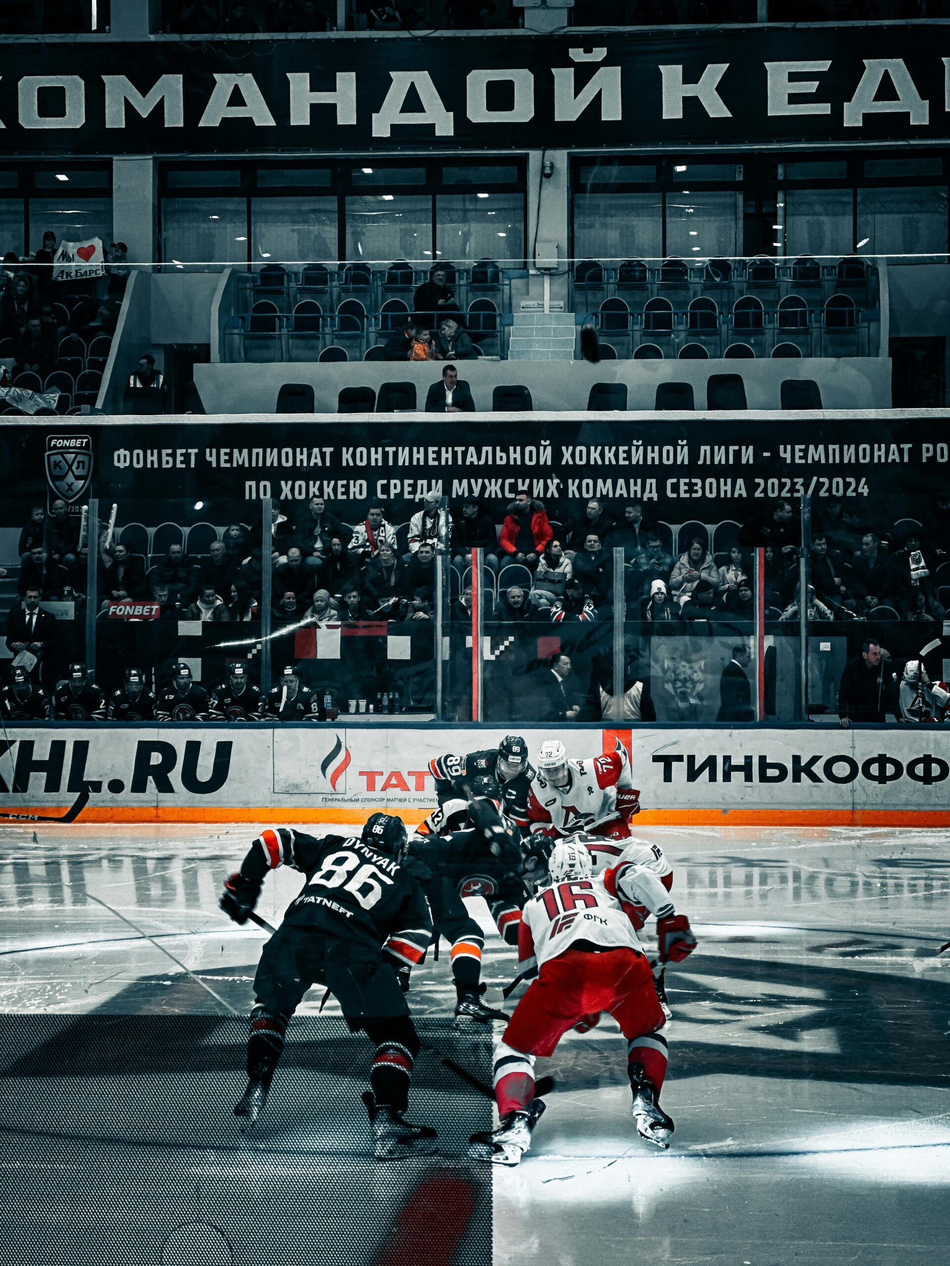 Players face off during a professional ice hockey match in an arena with the audience watching.