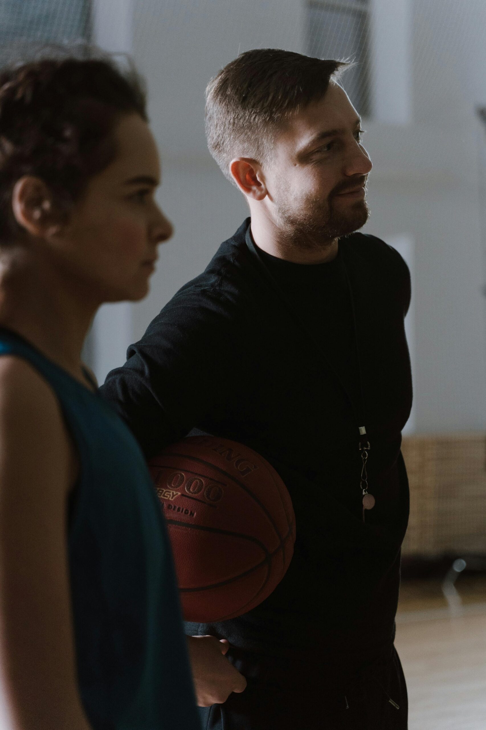 A basketball coach holding a ball while instructing a young player indoors.
